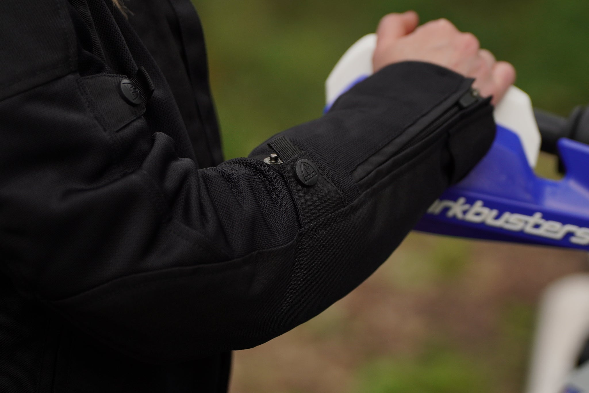 a close up of a woman's hand on a motorcycle mirror showcasing the sleeve of her black mesh jacket