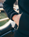 Person wearing a black jacket with a zipper, standing on a bridge.