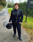 a smiling red haired woman motorcyclist wearing witches of wheels t-shirt, black jeans and mc jacket