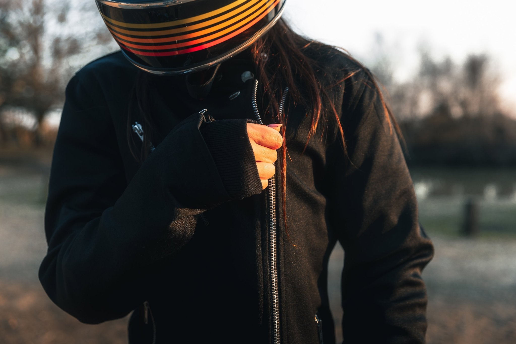 woman with a helmet zipping her Black retro style woman's motorcycle jacket with silver zip details
