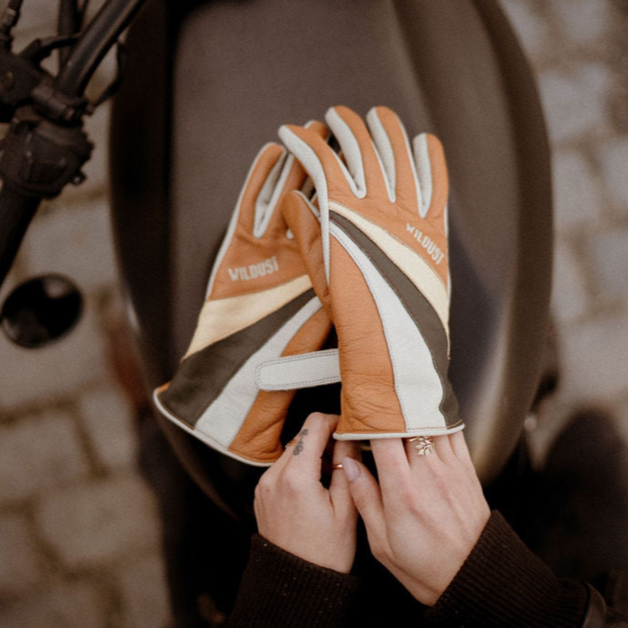 women&#39;s hands over a motorcycle gas tank while putting  on colourful leather gloves from WILDUST