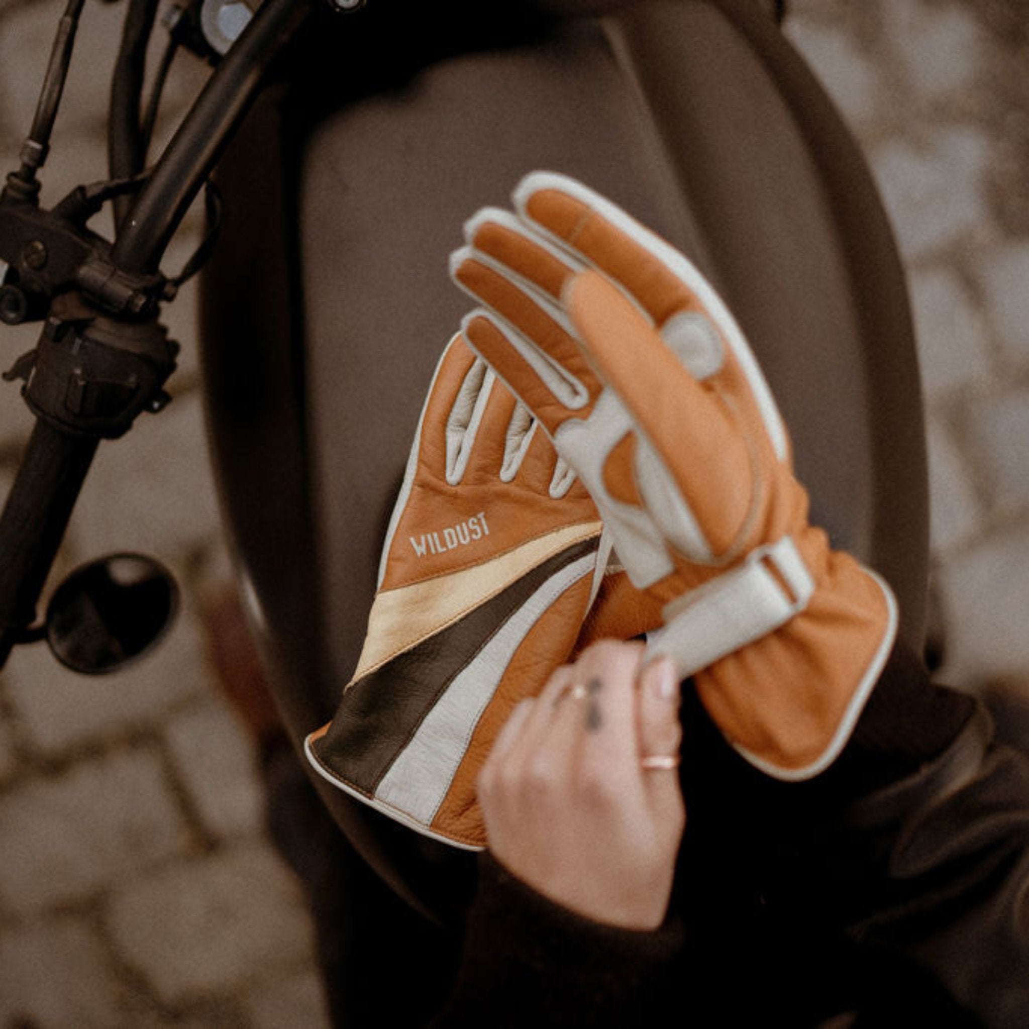 women&#39;s hands over a motorcycle gas tank while putting  on colourful leather gloves from WILDUST