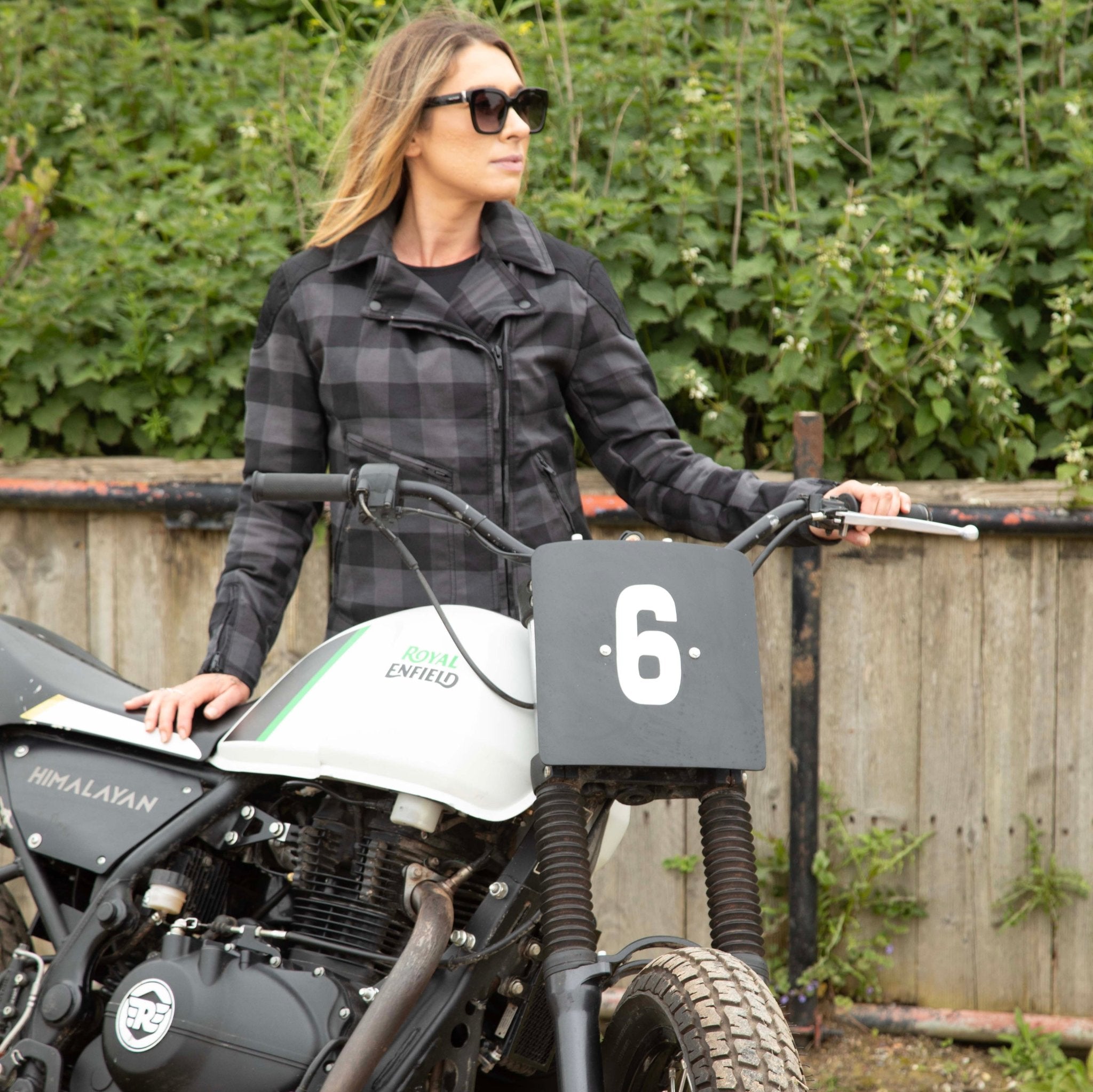 woman with sunglasses next to a motocross bike wearing a black &amp; grey flannel style women&#39;s jacket 