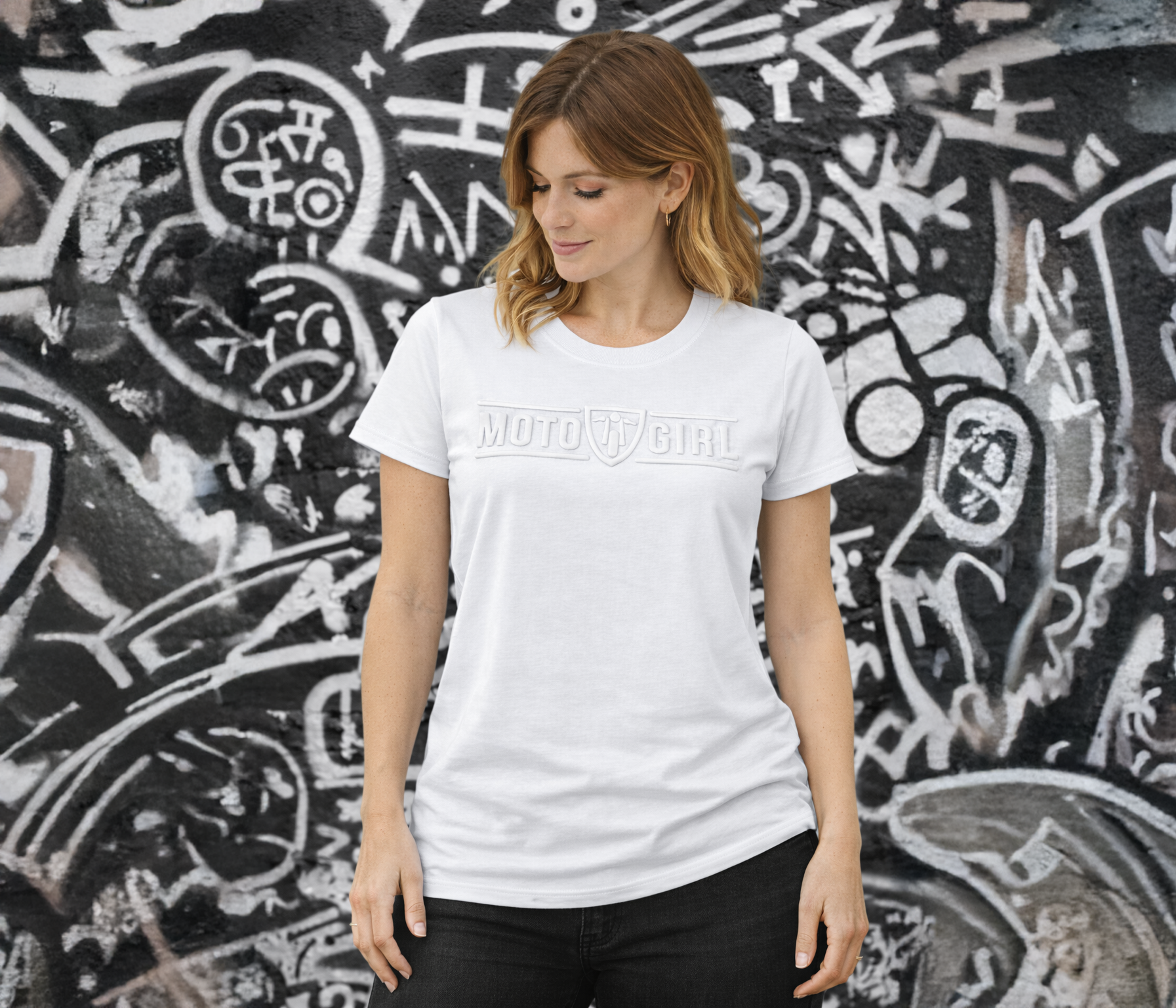 Woman wearing a white t-shirt with 'Moto Girl' text against a graffiti-covered wall.