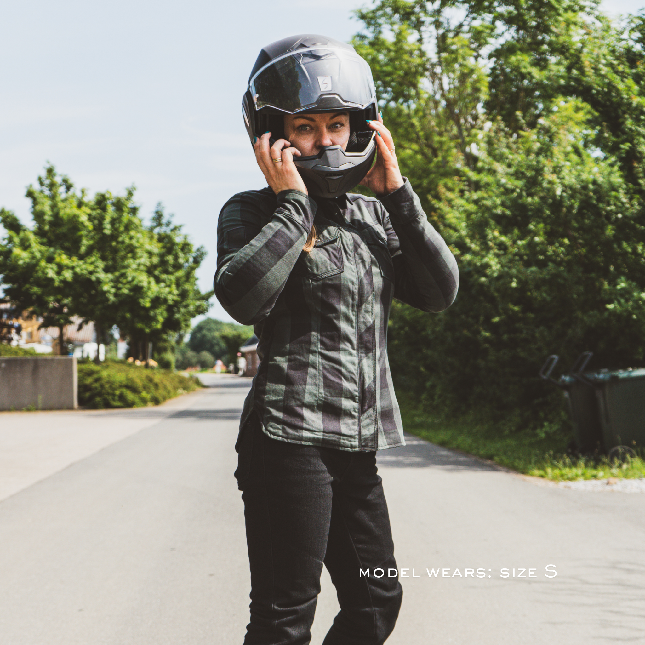 Person wearing a black helmet and green jacket on a road with trees in the background