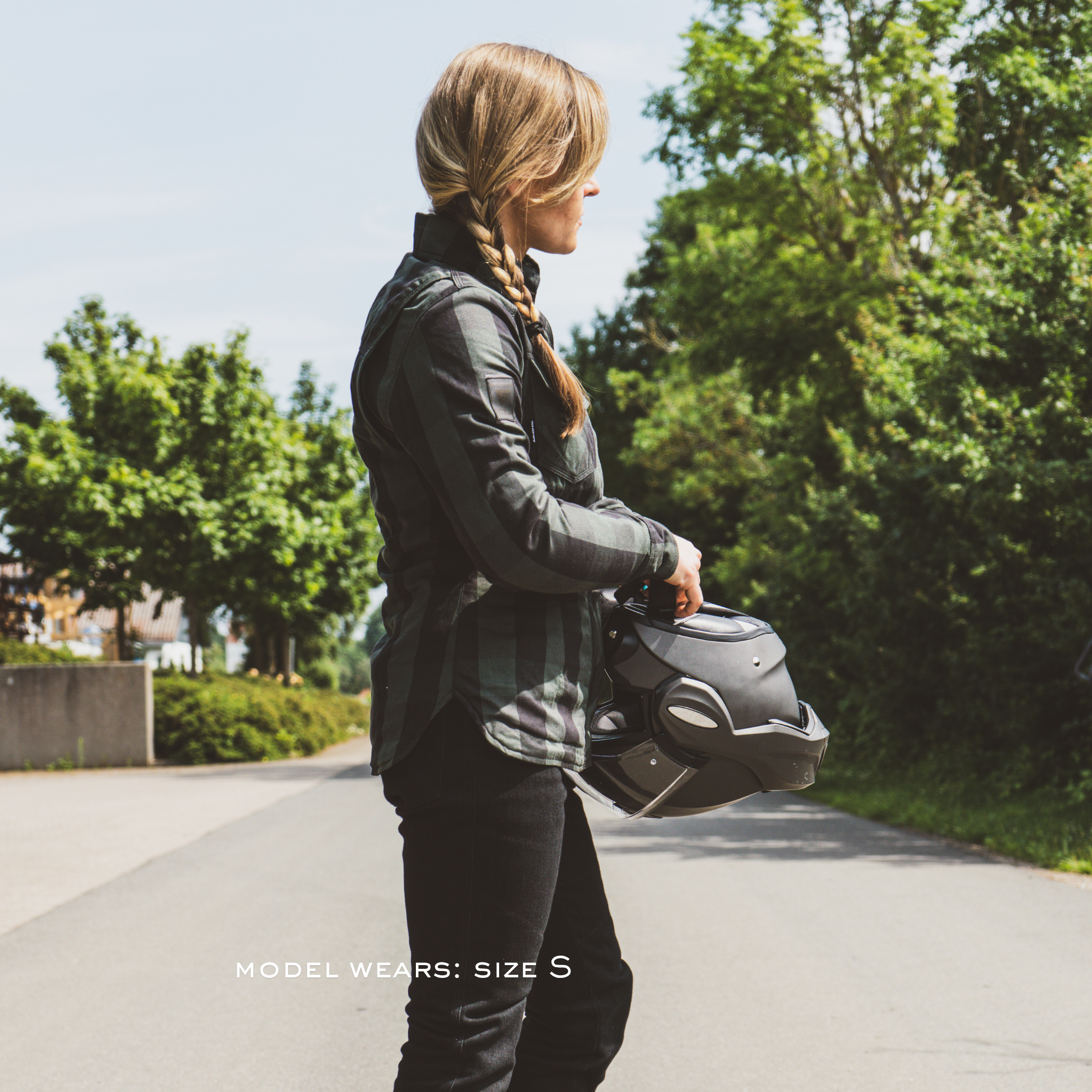 Person holding a helmet on a road with trees in the background
