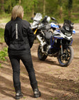 a blond woman standing back to the camera by her big motorcycle wearing a black mesh motorcycle jacket for women
