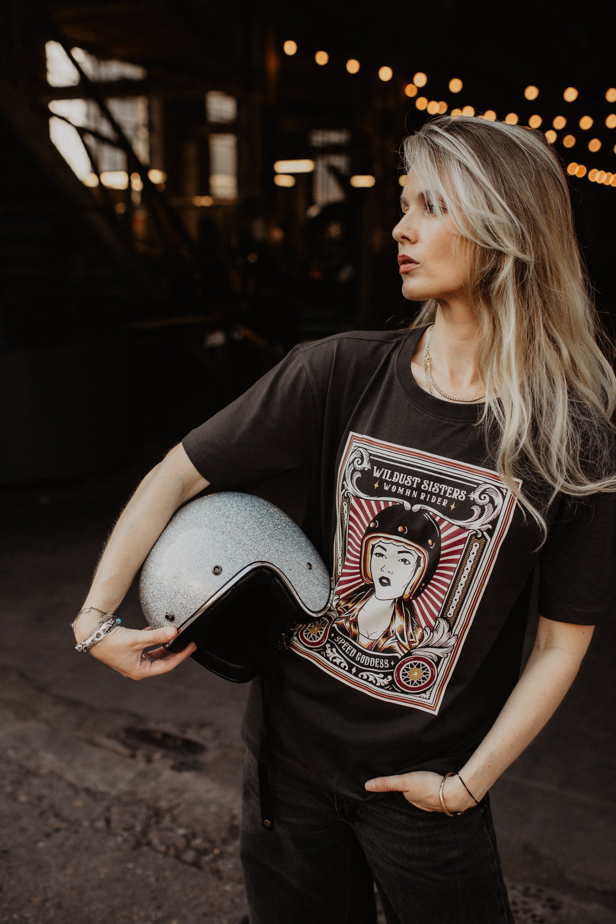 Woman with a Motorcycle helmet wearing a T-shirt with a women wearing a Motorcyclehelmet print and with the text &quot;Wild dust sisters woman rider&quot; and &quot;Speed Goddess&quot;