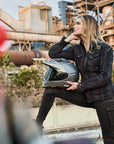A blond young woman dreaming while holding her motorcycle helmet wearing Black and grey lumberjack style women's motorcycle shirt from Shima