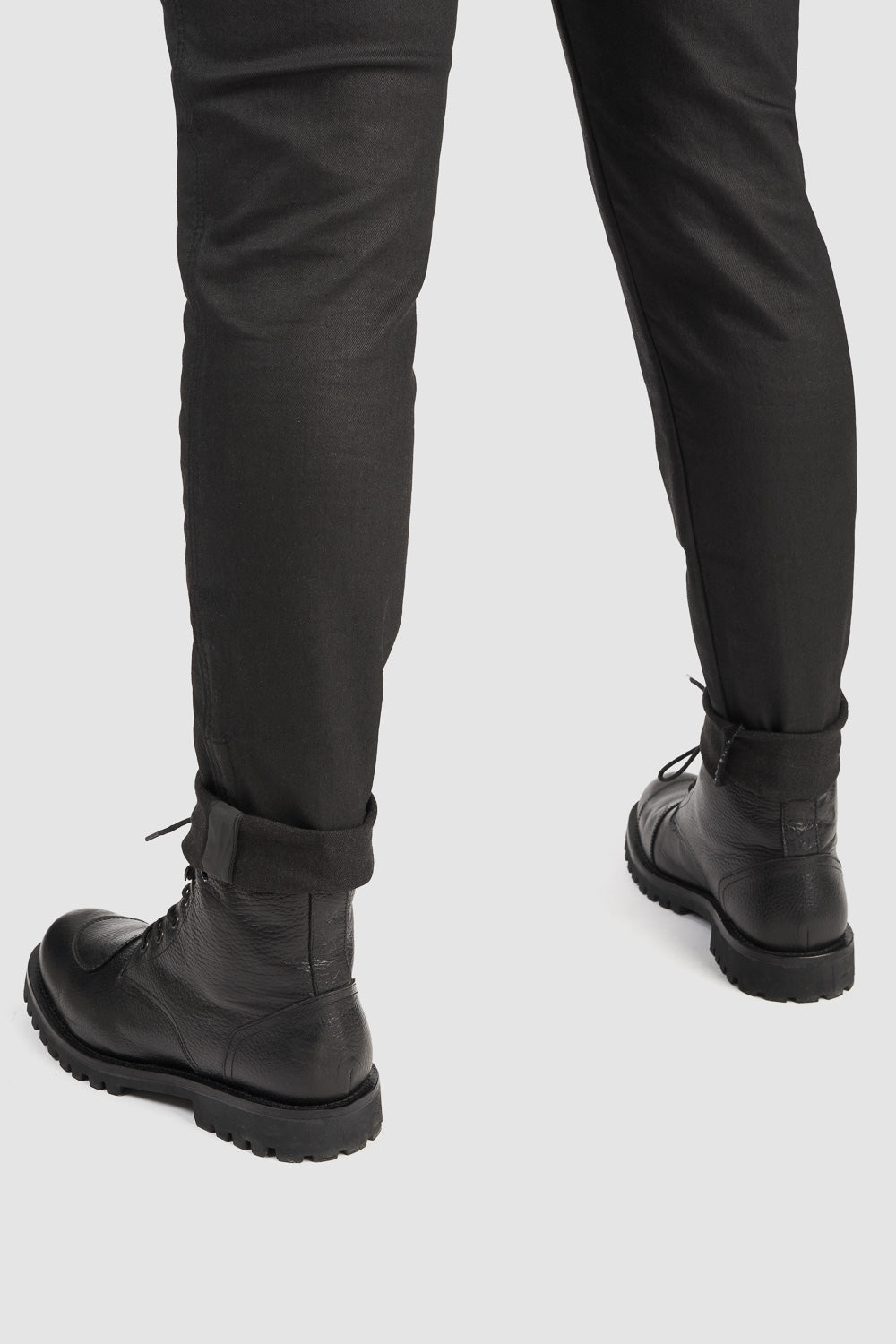 Person wearing black leather boots and black pants on a white background