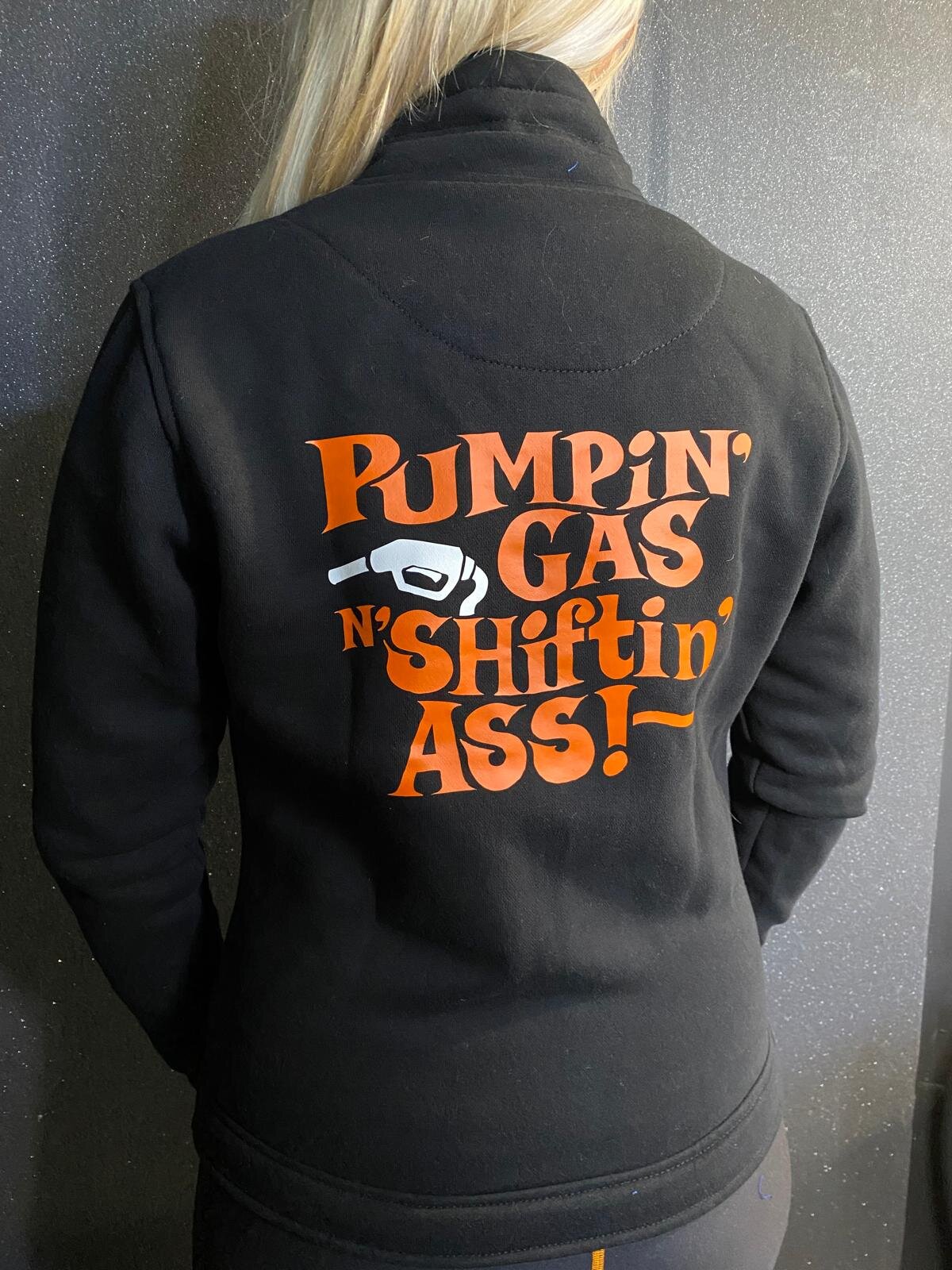 A woman wearing black lady sweatshirt with orange &quot;pumping gas shifting ass&quot;motive on the back