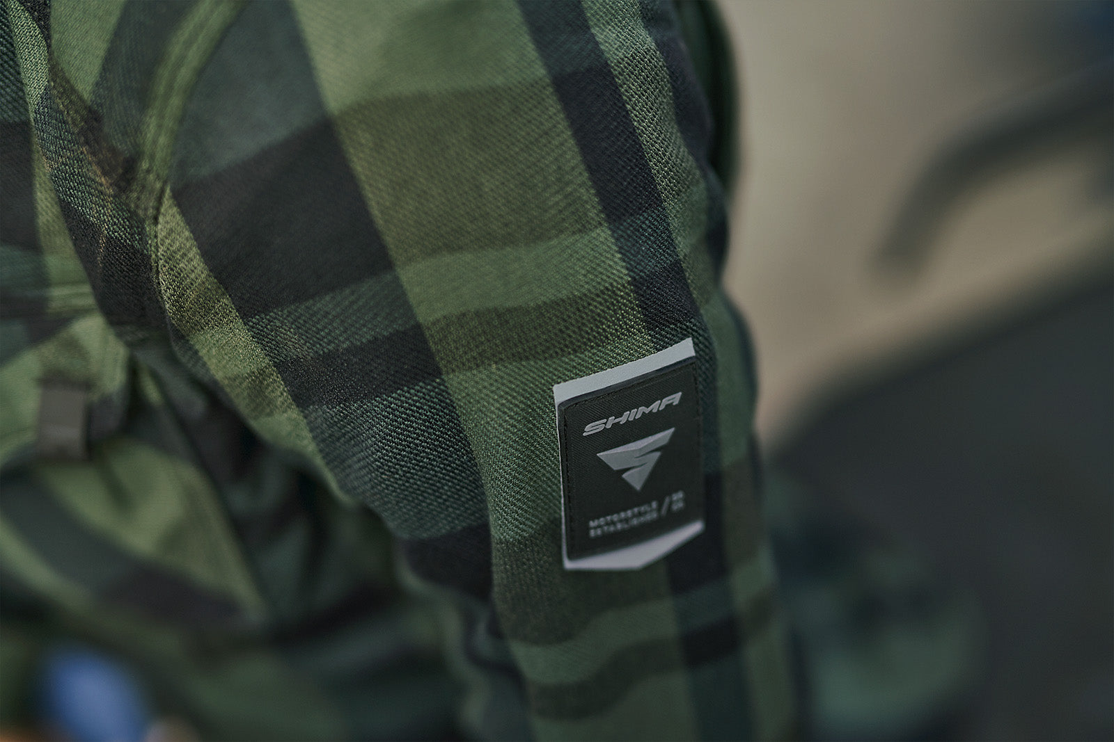 Green plaid fabric with a brand logo tag on a blurred background