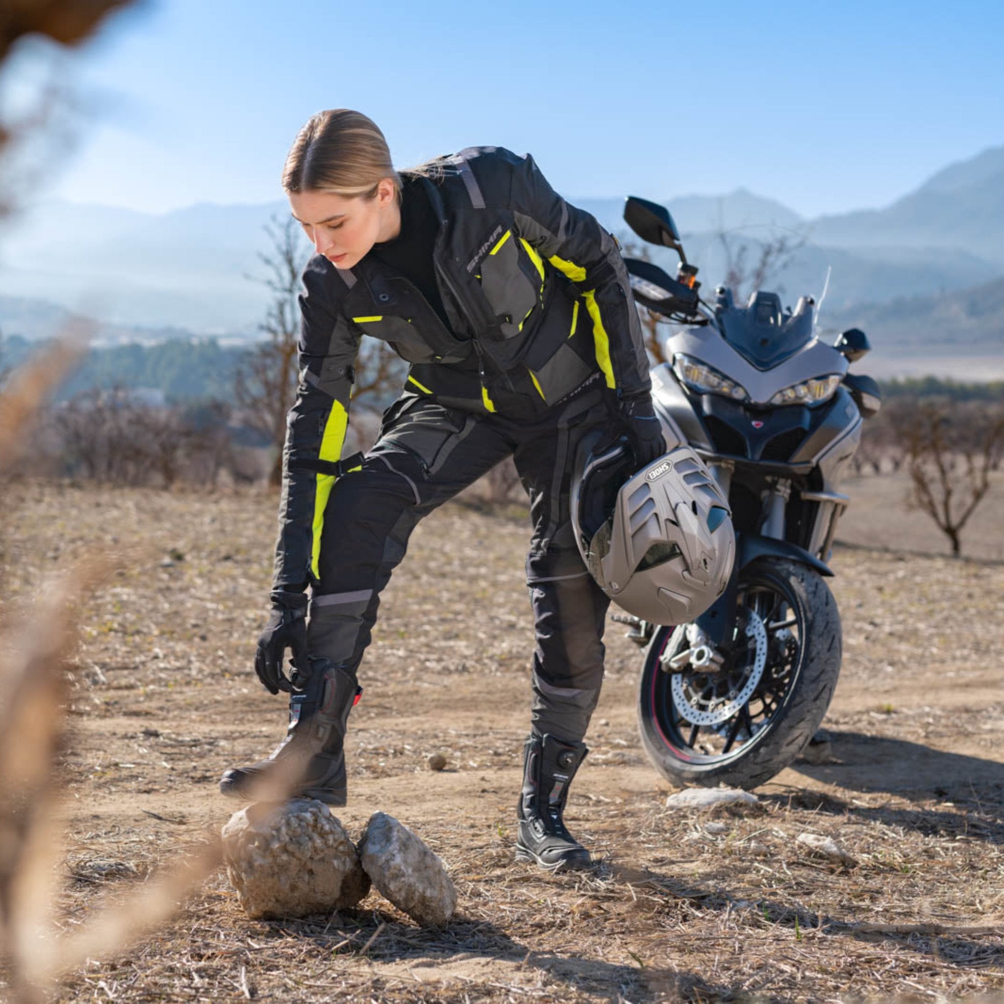 A woman closing her shoes wearing Black SHIMA touring motorcycle pants for women