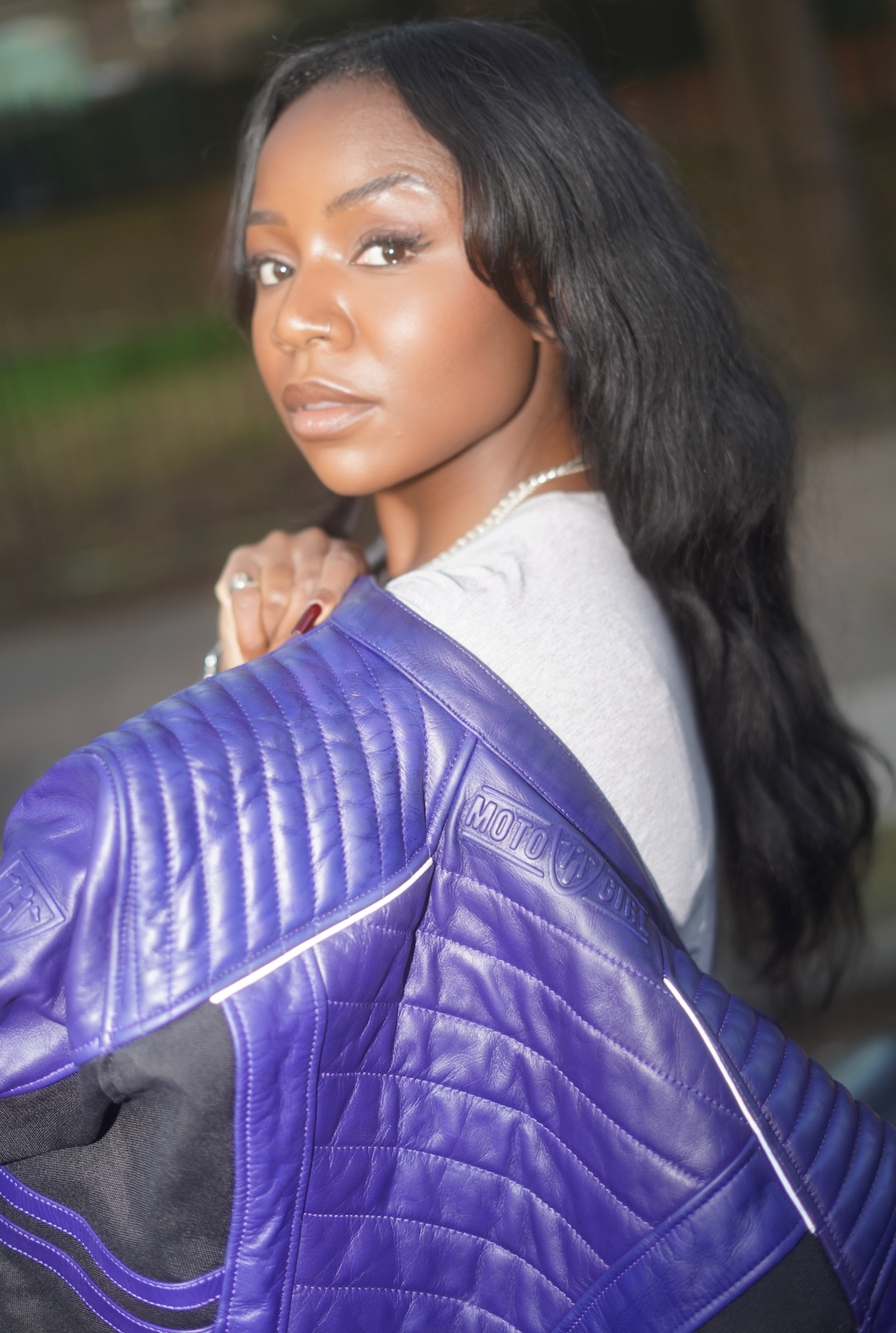 a black woman holding her purple motorcycle leather jacket on the shoulder