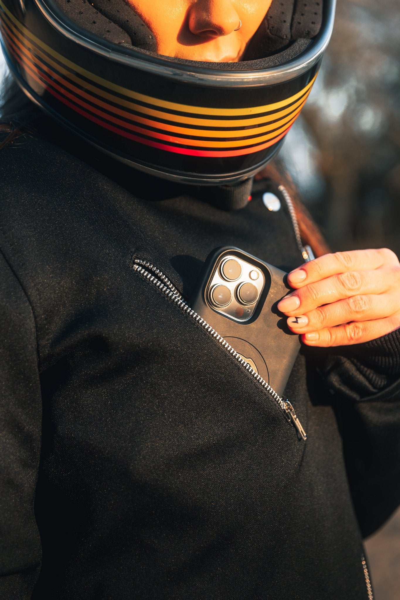 woman pitting her phone in a pocket of a Black retro style woman&#39;s motorcycle jacket with silver zip details