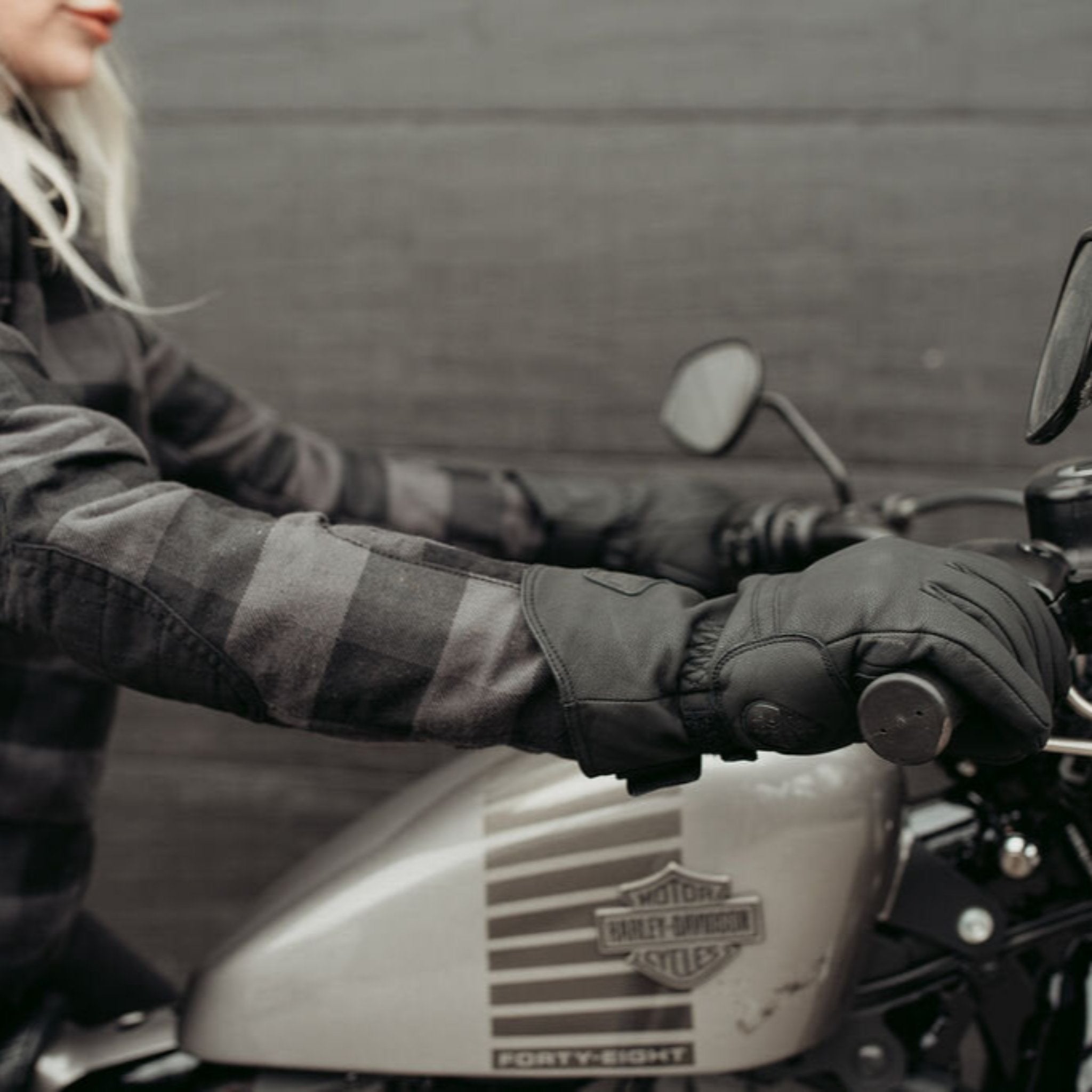 A blond woman on a Harley Davidson motorcycle wearing black Nandi winter motorcycle gloves from Motogirl.