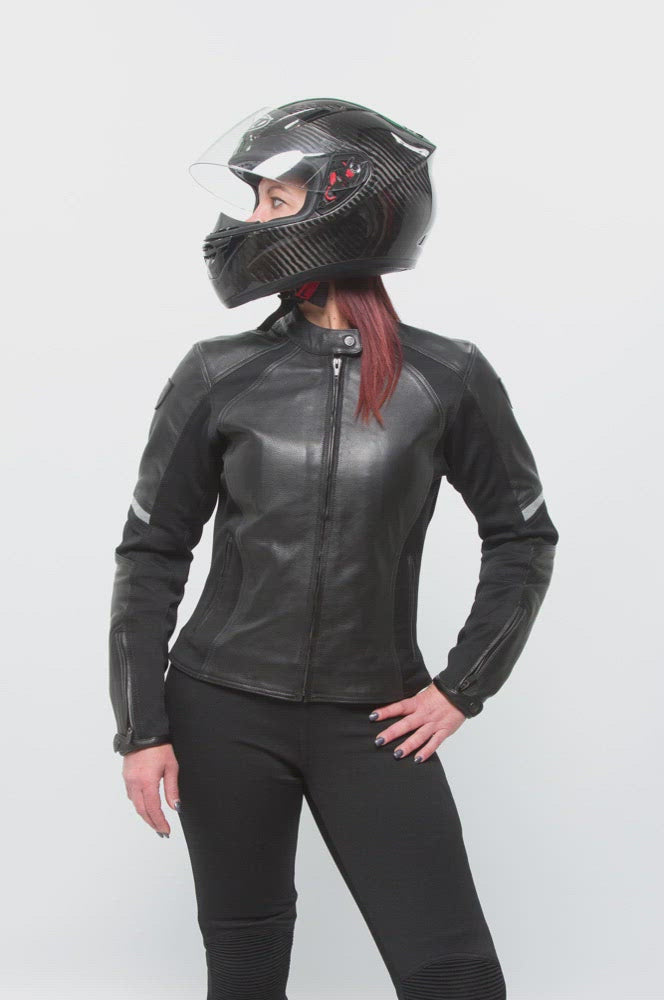 A red-haired woman wearing a helmet posing in a black leather women's motorcycle jacket with reflectors from Moto Girl