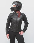 A red-haired woman wearing a helmet posing in a black leather women's motorcycle jacket with reflectors from Moto Girl