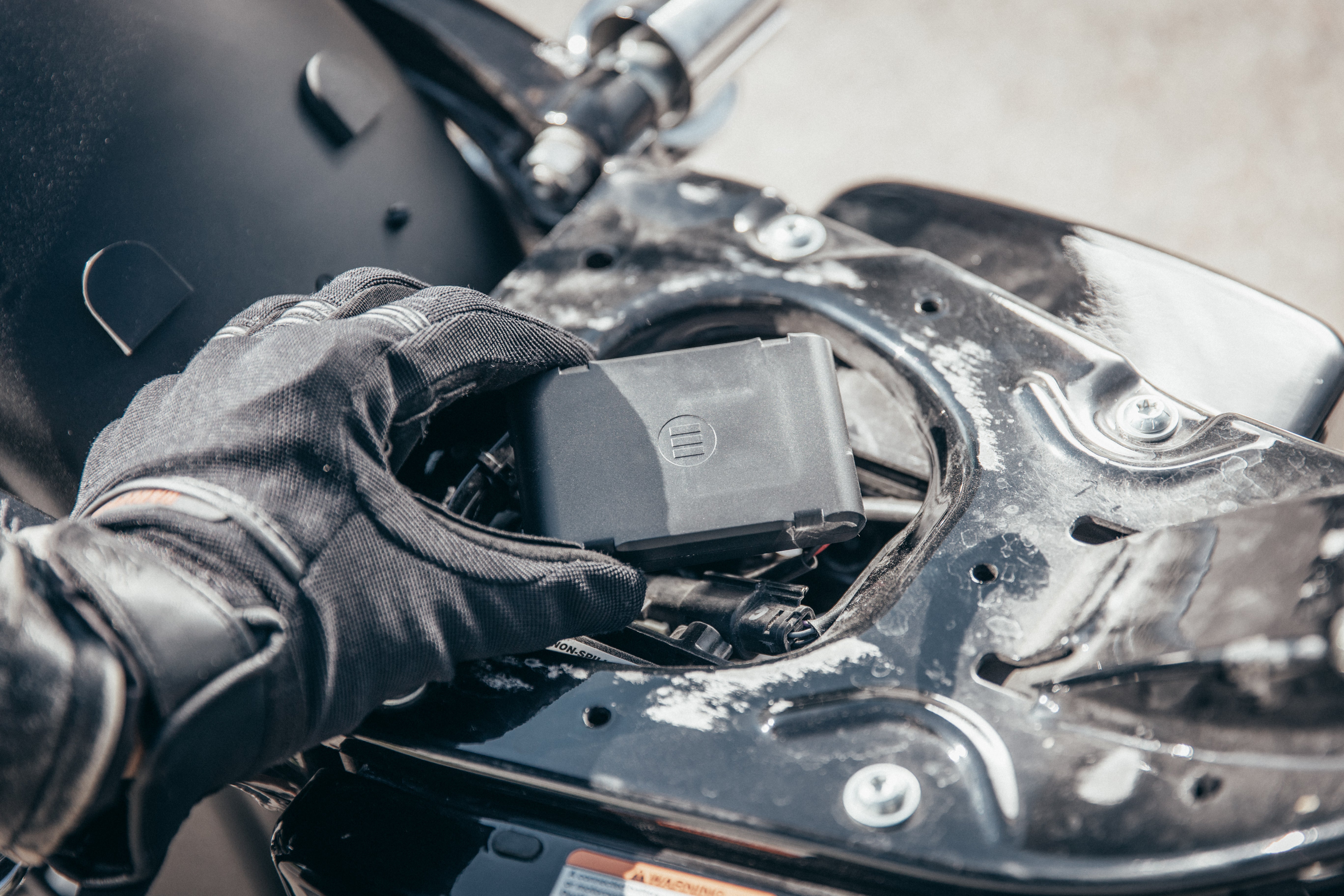 A motorcyclist&#39;s hand placing MoniMoto Motorcycle black and small GPS tracker into the motorcycle