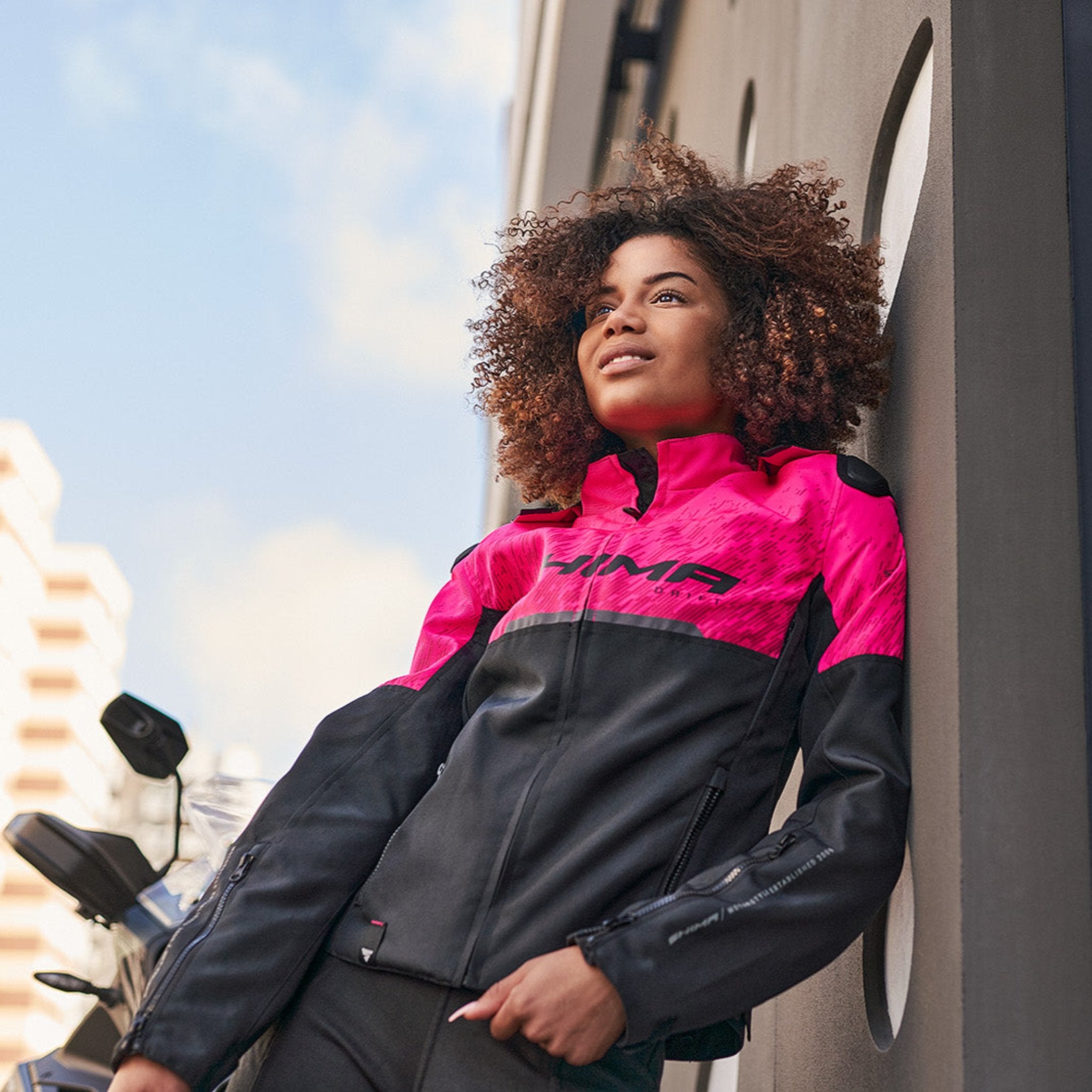 A young woman by a motorcycle wearing pink DRIFT motorcycle jacket from Shima