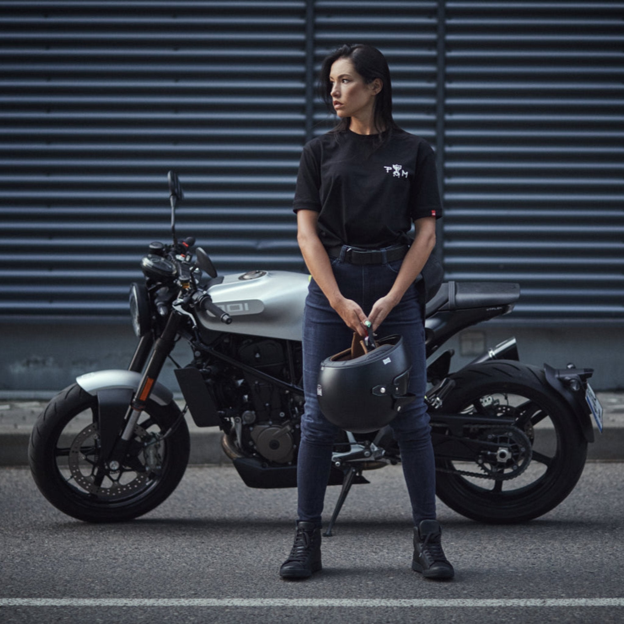 A young woman standing by her motorcycle wearing blue motorcycle jeans