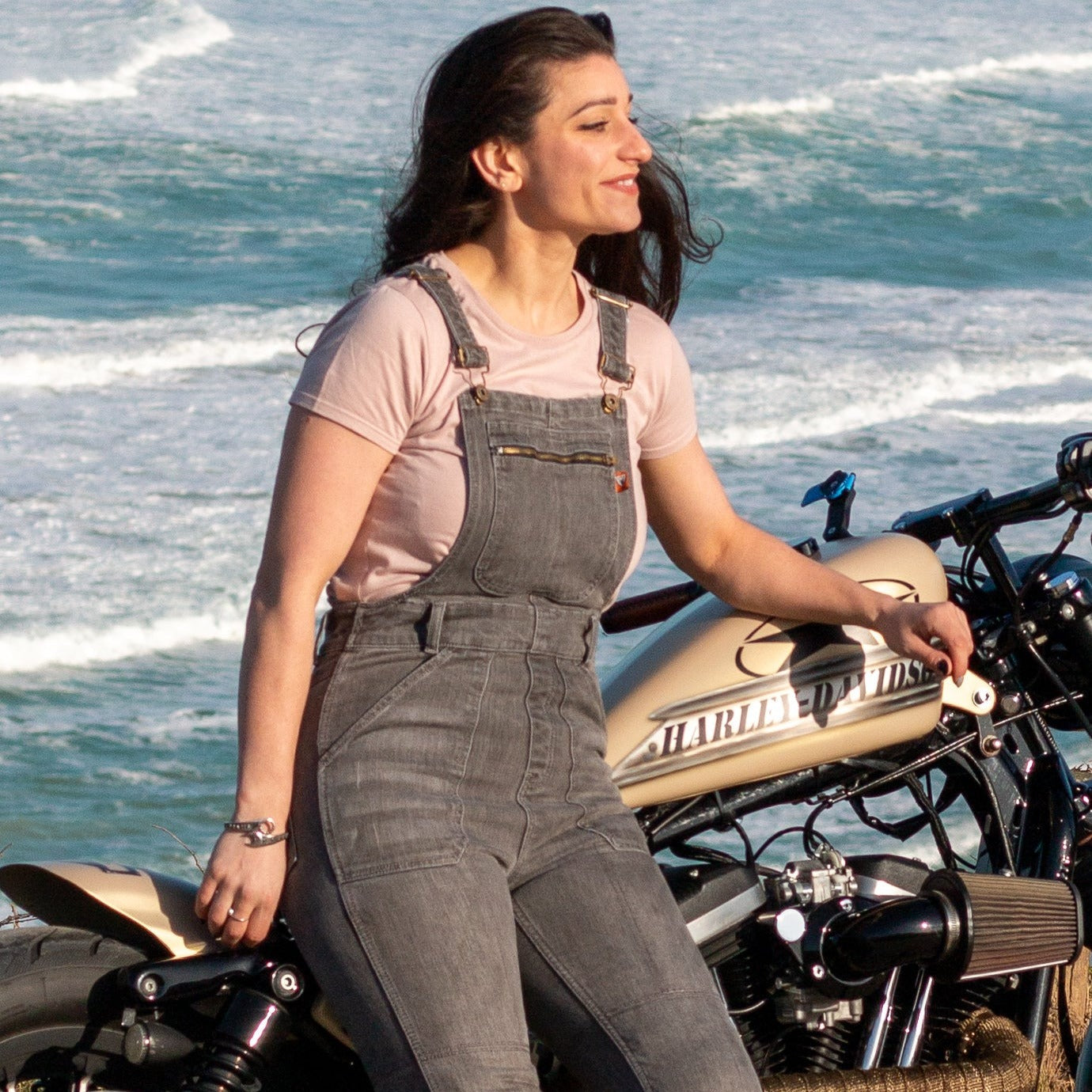 A woman by the beach with her motorcycle wearing grey women&#39;s motorcycle overall from Moto Girl
