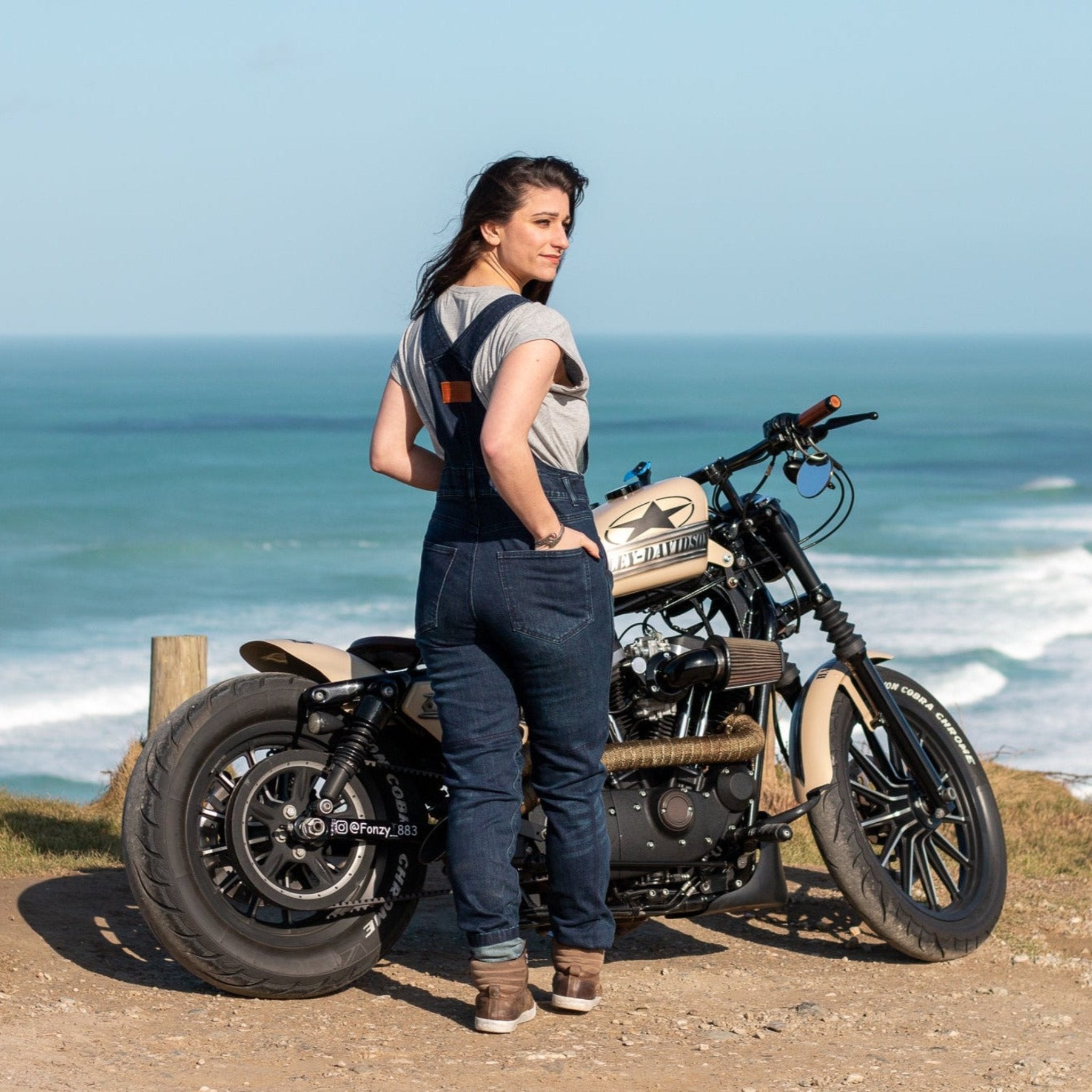 A woman by the beach with her motorcycle wearing blue women&#39;s motorcycle overall from Moto Girl