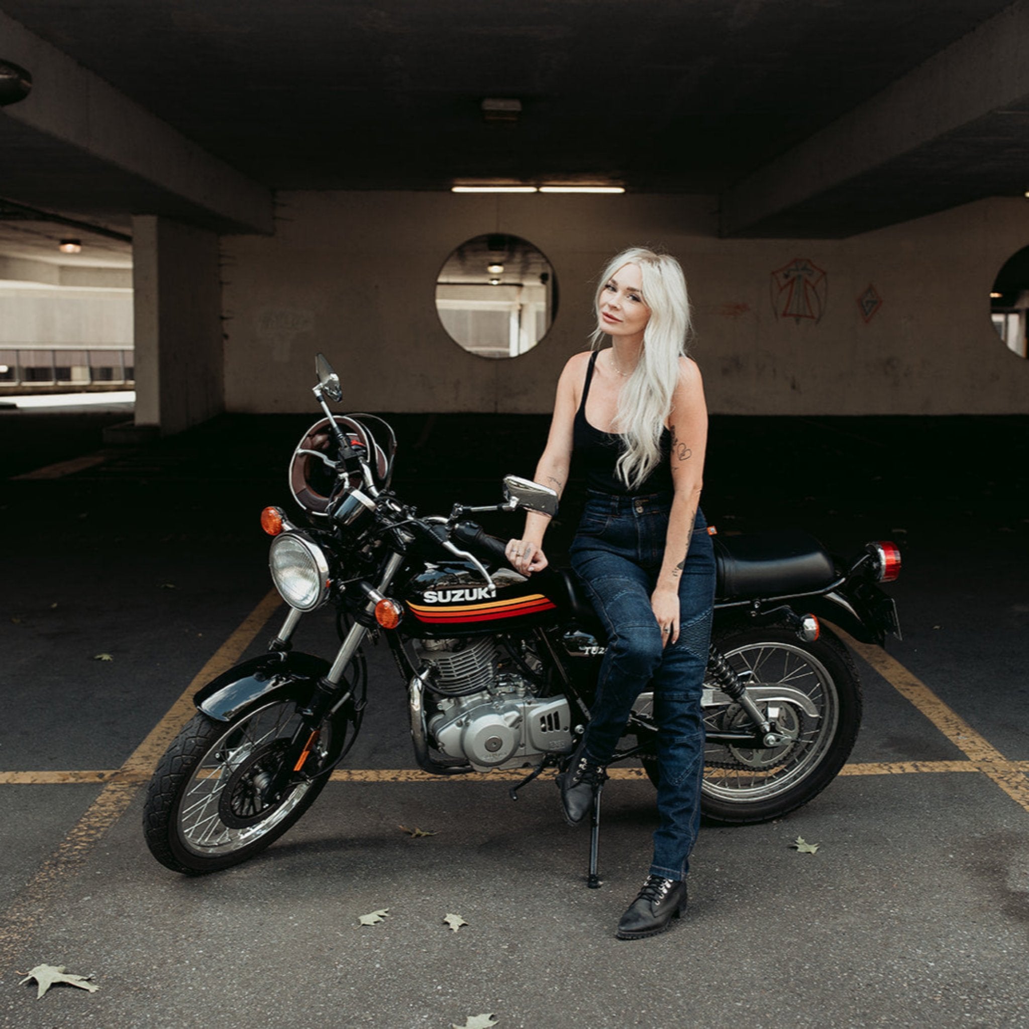 A tattooed woman on her Suzuki motorcycle wearing black lady motorcycle jeans from Moto Girl.