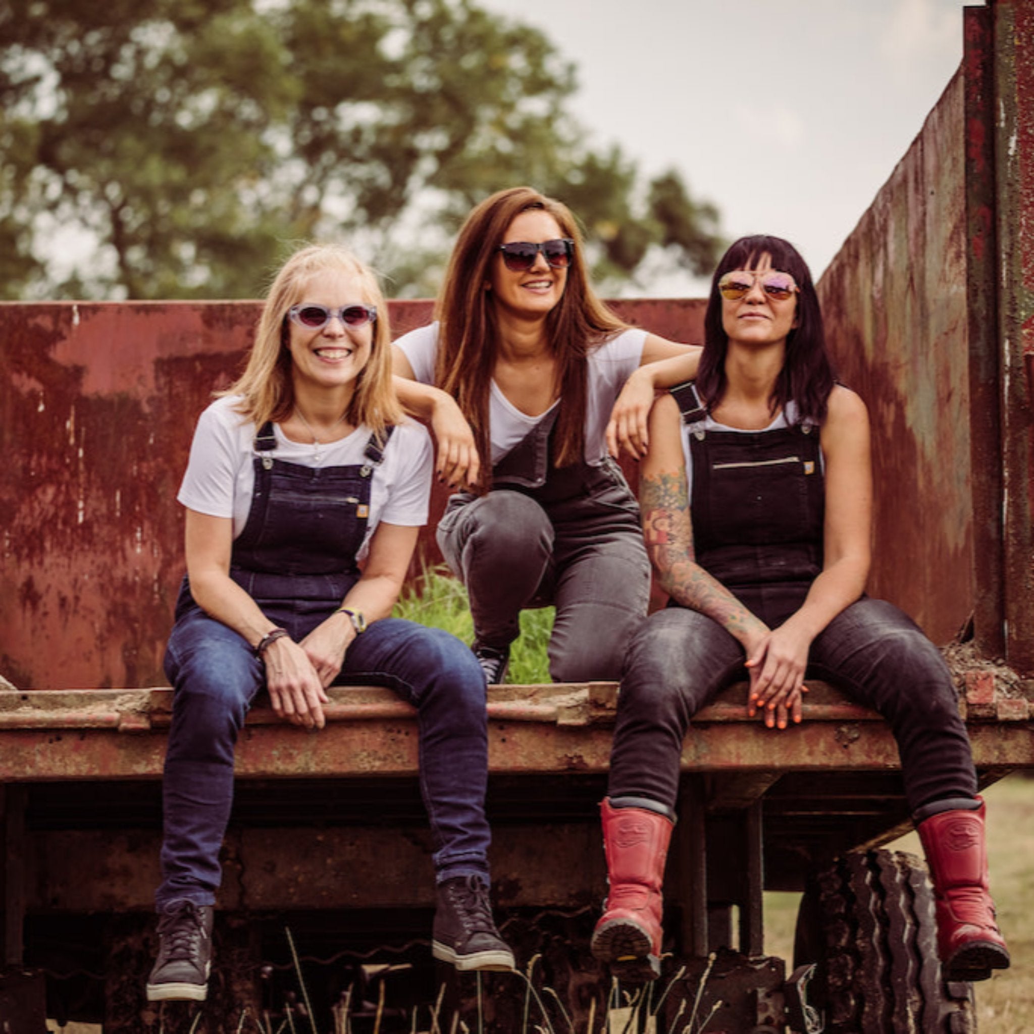 Three women wearing motorcycle overalls siting on the back of a truck