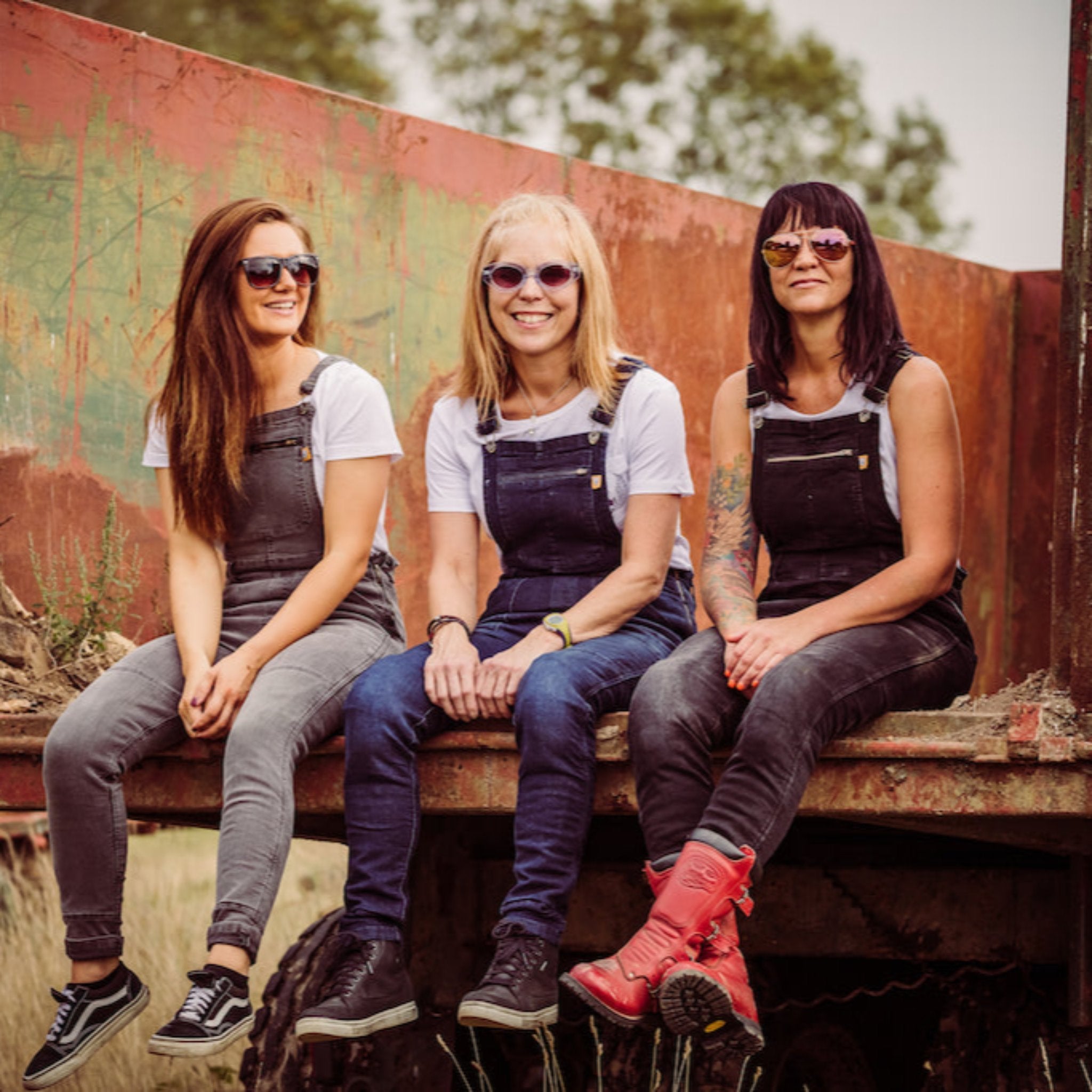 Three women wearing motorcycle overalls siting on the back of a truck