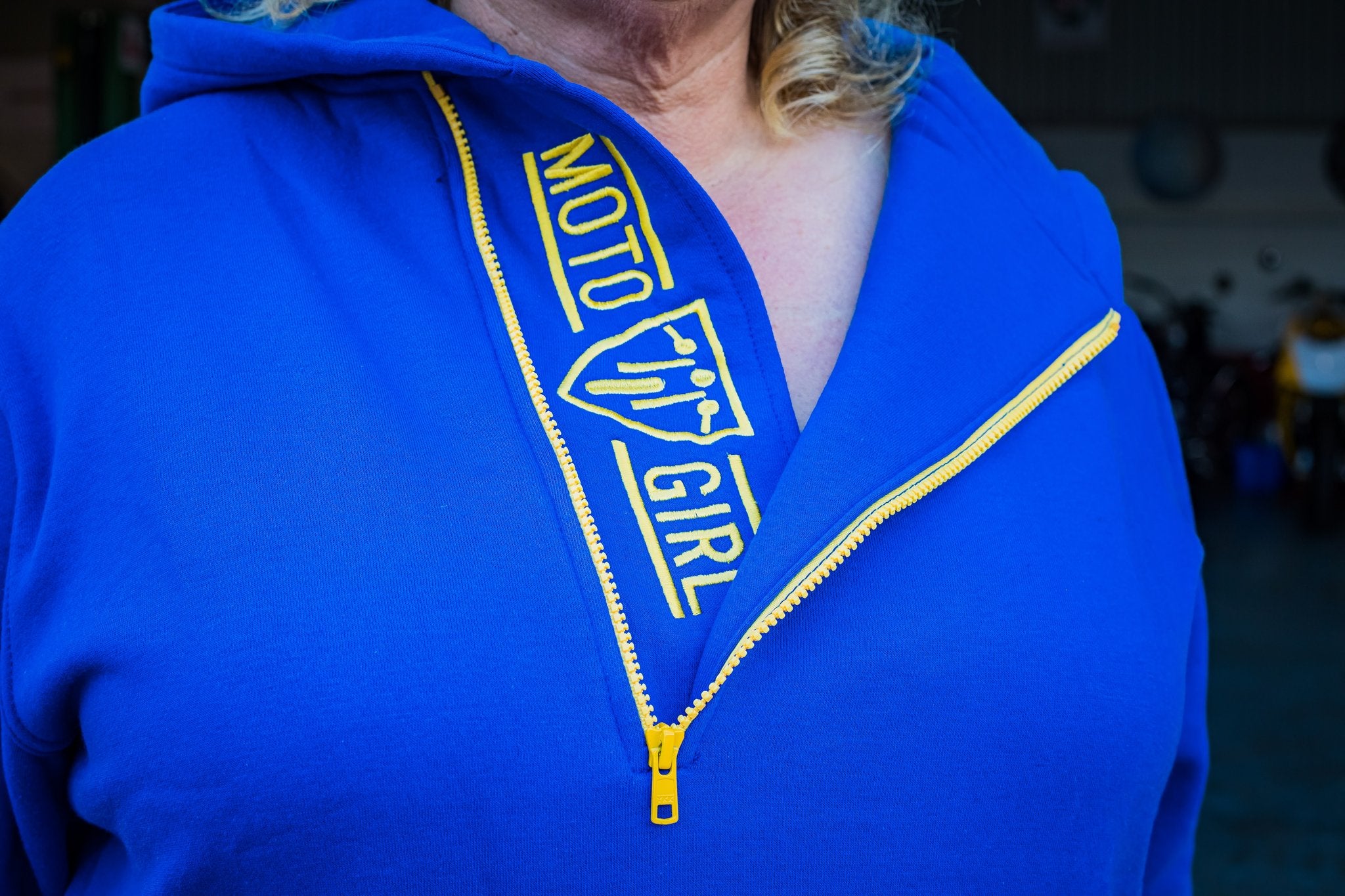 A blond woman wearing blue and yellow motorcycle hoodie