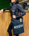 A woman leaning on the shop counter wearing black women's garage suit  from MotoGirl and a MotoGirl bag