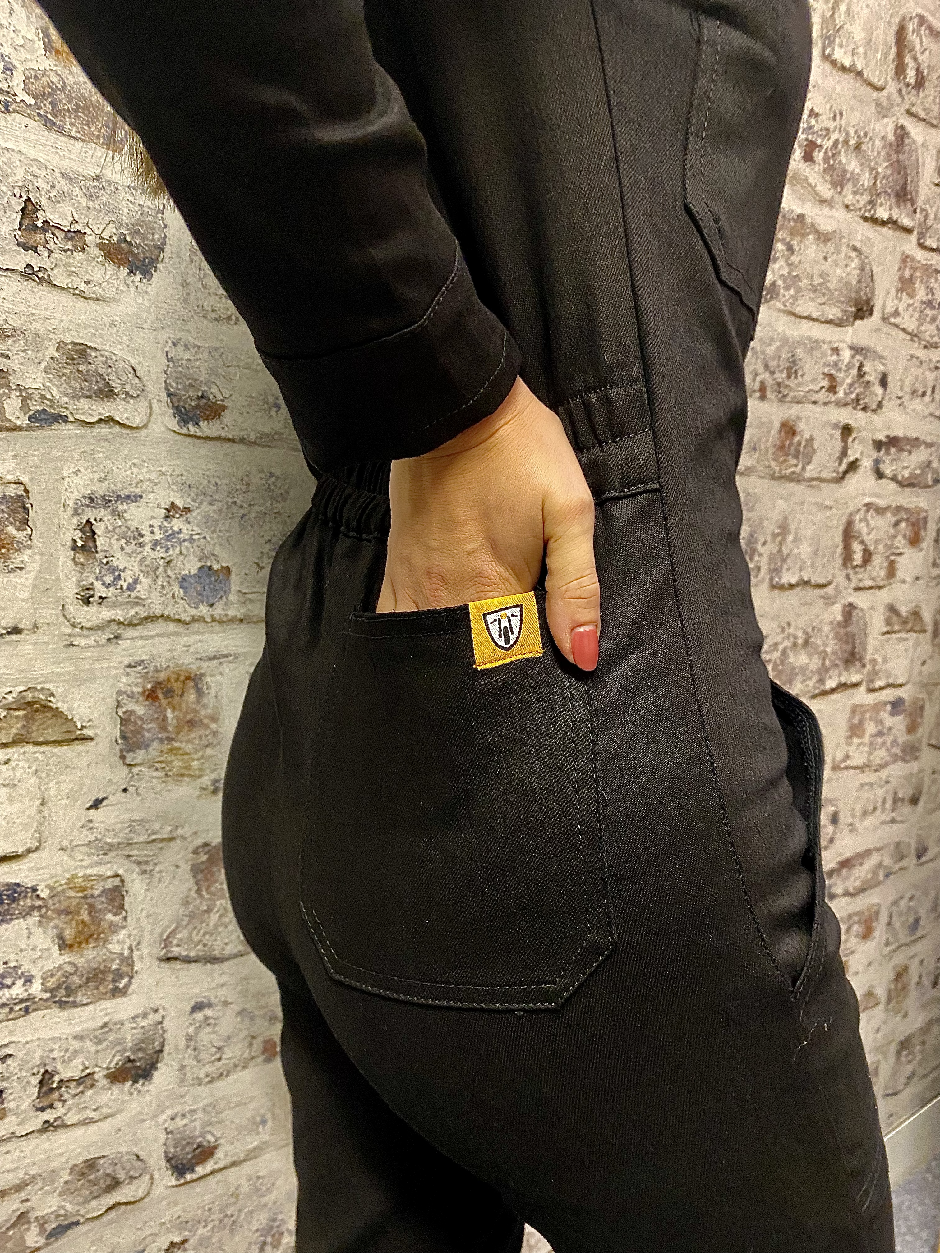 A close up of a woman holding her hand in the back pocket of black women&#39;s garage jumpsuit from MotoGirl