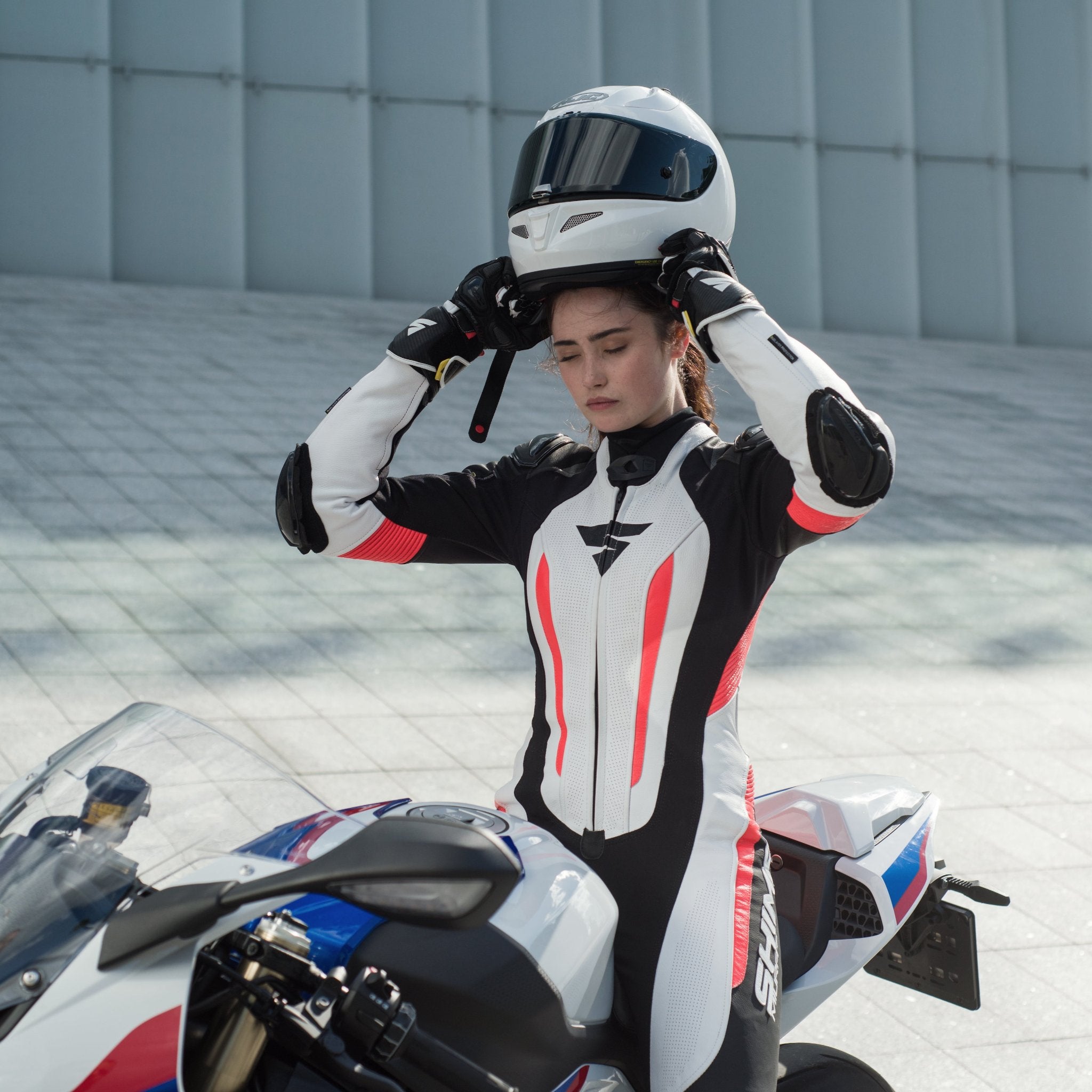 A woman putting her helmet on and wearing Women&#39;s racing suit MIURA RS in black, white and fluo from Shima 