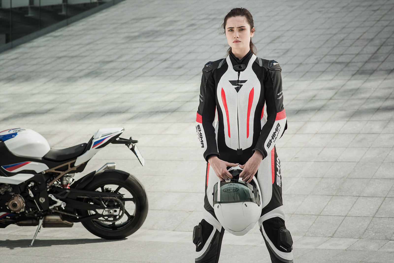 A young woman standing near a motorcycle wearing Women's racing suit MIURA RS in black, white and fluo from Shima 