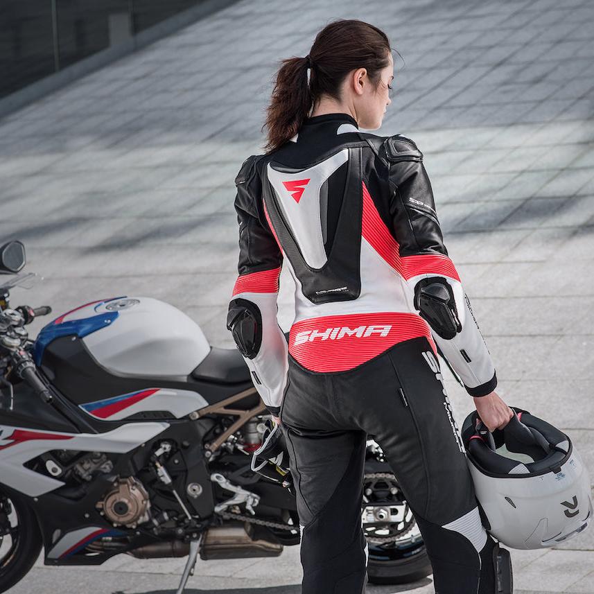 A woman standing near her motorcycle wearing Women&#39;s racing suit MIURA RS in black, white and fluo from Shima 