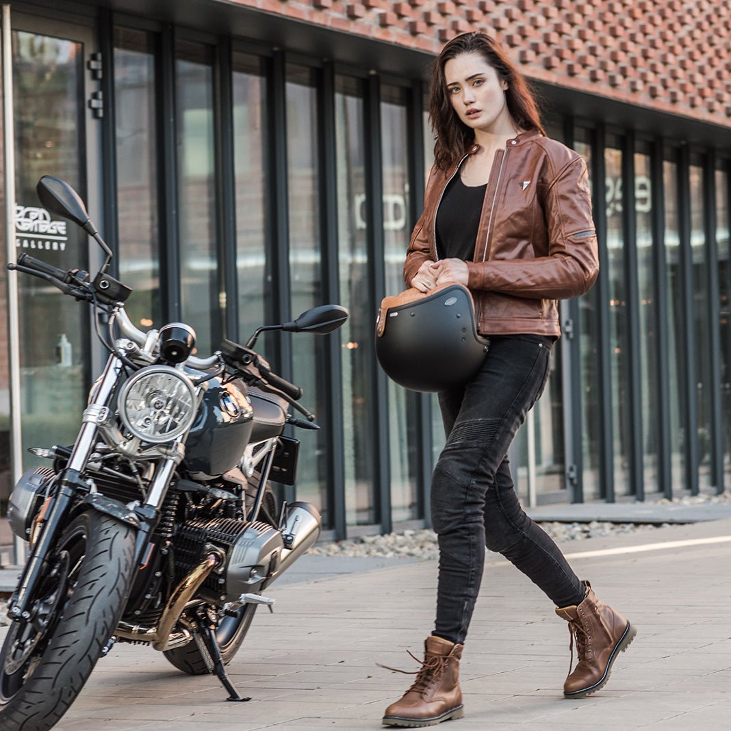 A young woman by a motorcycle wearing brown motorcycle leather jacket and brown women motorcycle boots from Shima