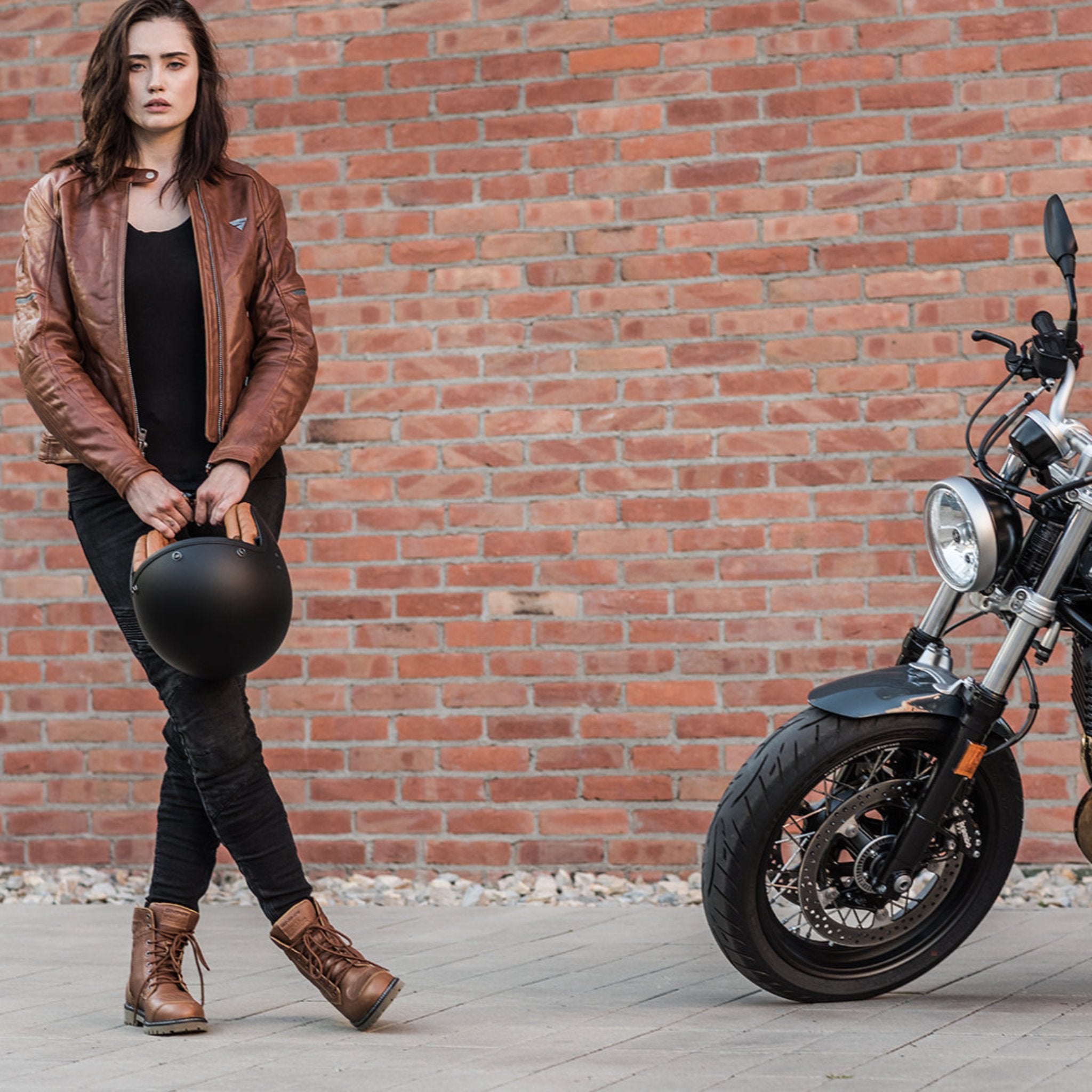 A young woman by a motorcycle wearing brown motorcycle leather jacket and brown women motorcycle boots from Shima