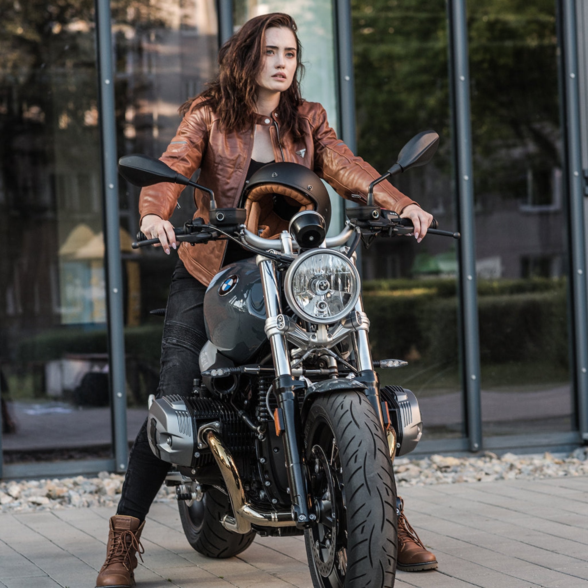 A young woman by a motorcycle wearing brown motorcycle leather jacket and brown women motorcycle boots from Shima