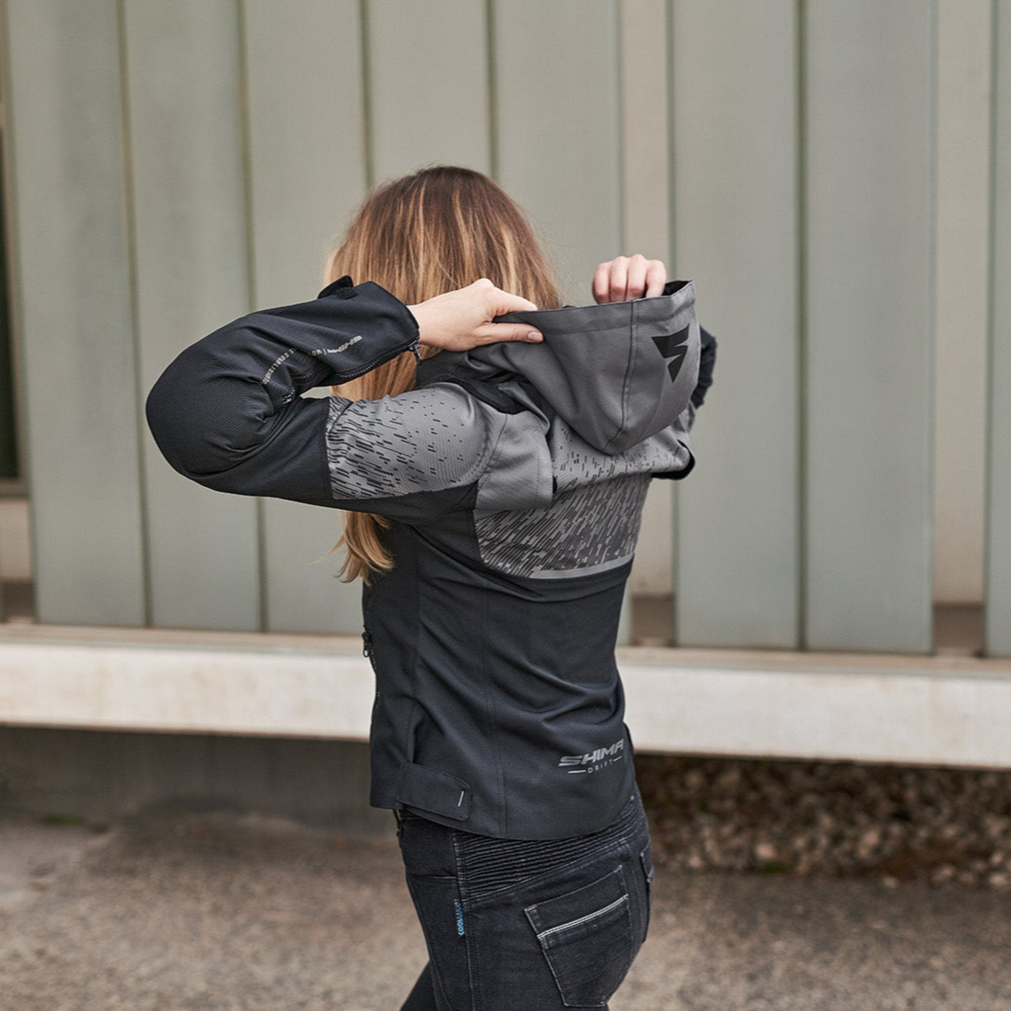 A woman putting a hood of a grey motorcycle jacket  from shima