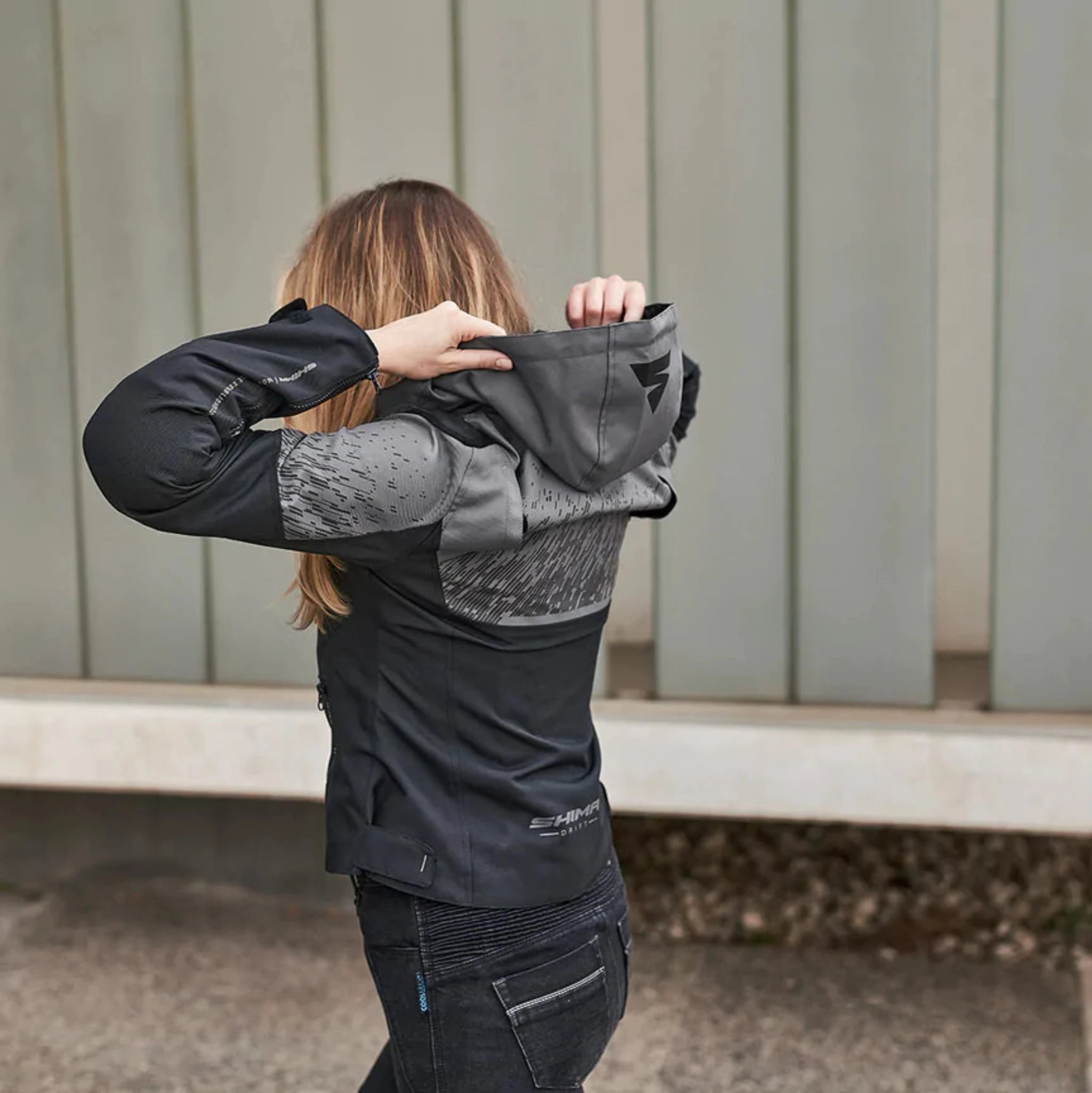 A woman is wearing a motorcycle grey jacket with a hood