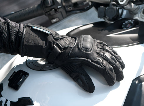 A  woman&#39;s hand with black waterproof motorcycle glove on a white motorcycle  tank 