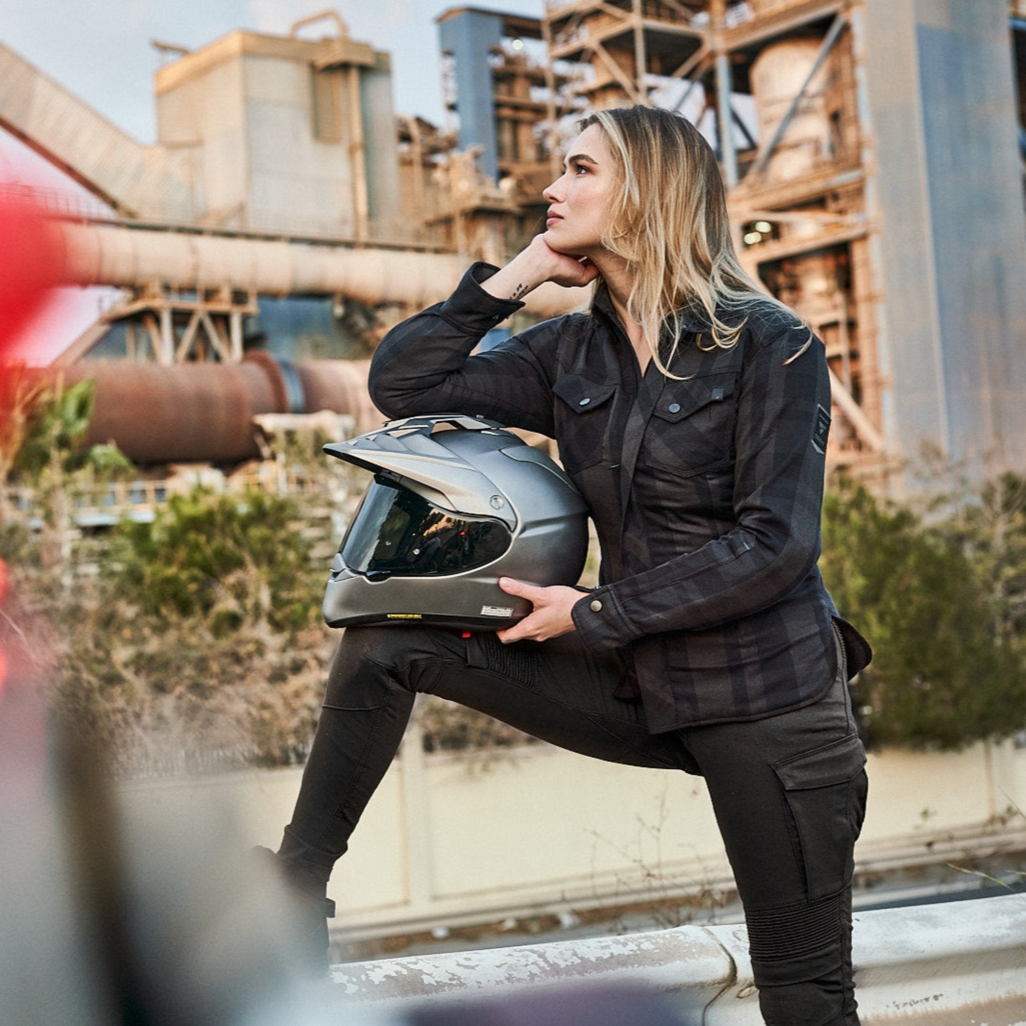 A young woman holding the helmet and wearing Khaki green women&#39;s motorcycle cargo pants GIRO from shima