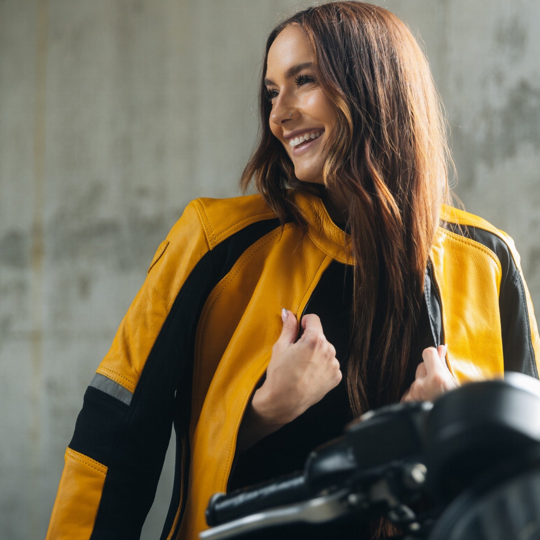 A young woman on her motorcycle wearing a red and black women&#39;s motorcycle jacket with reflectors on the sleeves.