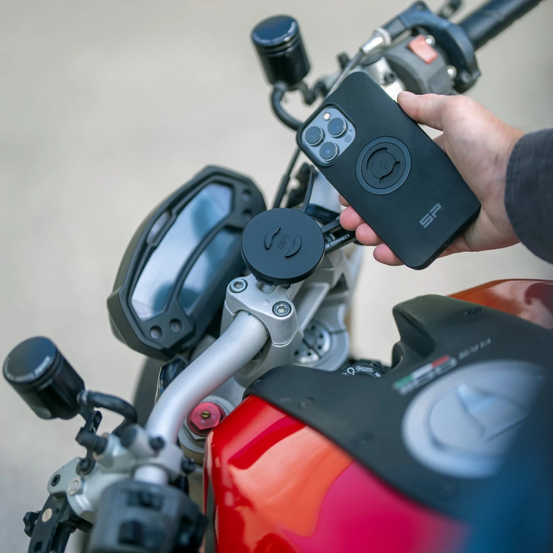 A phone being mounted with the SPC mounts  on a red motorcycle 